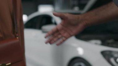 Kahverengi ceketli, tanınmayan bir kadın müşterinin, araba sorununu el sıkışarak çözdüğü için teknisyene teşekkür ederken, tamirhaneden tamir edilen arabayı alırken çekilmiş yakın plan fotoğrafı.
