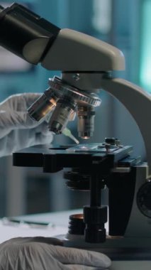 Laboratuvar deneyi sırasında, kimliği belirsiz kadın bilim adamının, kaydıraktaki doku örneğine bir damla sıvı ekleyerek objektif göz merceğini büyütmeyi seçmek için kaldırdığı dikey yakın plan fotoğrafı.