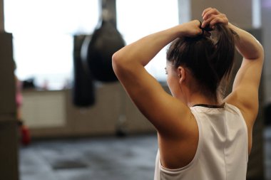 Uzun saçlı, at kuyruğu yapan ve spor salonunda boks antrenmanından önce saçını bantlayan genç bir sporcunun arka planı.