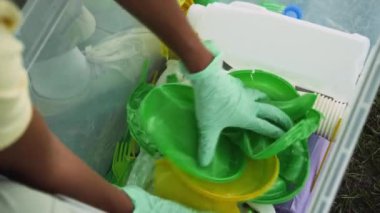 Tanımlanamayan kadın çevreci aktivistin, çöp konteynırından renkli plastik tabak ve fincanları çıkartıp takım arkadaşına geçirdiği yakın çekim görüntüleri.
