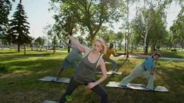 Tam orta yaşlı yogacı pozu, yaşlılar için yoga dersleri, yan açı pozu, ya da güneşli yaz gününde yeşil parkta paspaslar üzerinde utthita parsvakonasana.