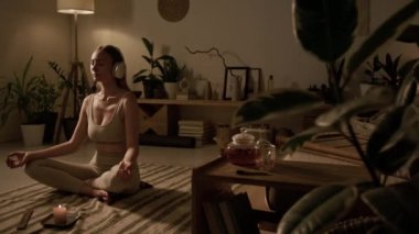 Bej bluzlu, ince beyaz kadın ve Sukhasana 'da yoga taytı giymiş, kablosuz kulaklık takmış, meditasyon yapıyor, elleriyle Gyan Mudra' yı işaret ediyor.