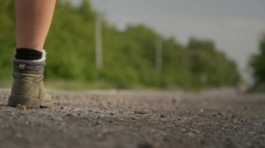 Yürüyüş botları ve çorapları giyen, sırt çantası taşıyan, kırsal yolda yürüyen ve otostop çeken, tanınmayan genç bir kadının çıplak bacaklarının orta derecede yakın plan çekimi.