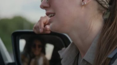 Yakışıklı araba sürücüsüyle sohbet eden, dikiz aynasından yansıyan, tatil yerine yolculuk yapan, rotayı tartışan, gülümseyen ve flört eden beyaz bir kadının yakın çekimi.