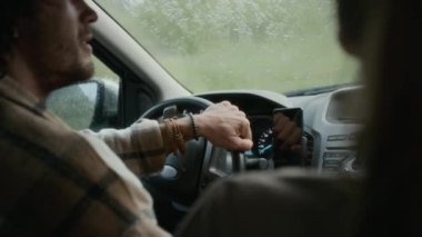 Sağanak yağmurda araba süren, tatile giden, canlı sohbetler yapan, birbirine bakan ve gülümseyen genç beyaz erkek ve kadının orta boy yakın çekimleri.