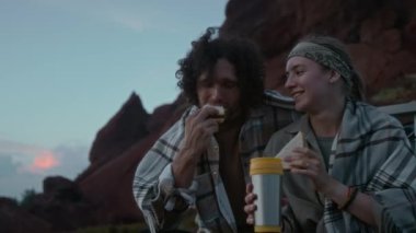 Akşamları uzun bir araba yolculuğu sırasında kamyonun bagajında oturup sandviç yerken, mataradan çay içerken, günbatımının keyfini çıkarırken, sohbet ederken ve gülümserken orta boy beyaz bir çift fotoğrafı.