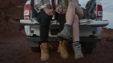 Kamyon bagajında birlikte oturmuş, çay içip dinlenirken, çölde tatil yaparken tanınmayan genç adam ve kadının orta boy sallanan bacakları.