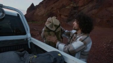 Kafkasyalı genç çiftin çölde dağın önüne park etmiş bir kamyonetin bagajından sırt çantalarını alıp geceleri kamp yapmak için vahşi doğada yalnız başlarına gezerken çekimleri tam olarak devam ediyor.