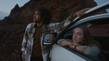 Düşünceli genç beyaz bir çiftin orta boy portresi vahşi güzellik dağlarında gün batımını hayranlıkla seyrediyor kız pencereye yaslanıyor, erkek yanında duruyor yaz tatillerinde şehir dışında seyahat ediyor.