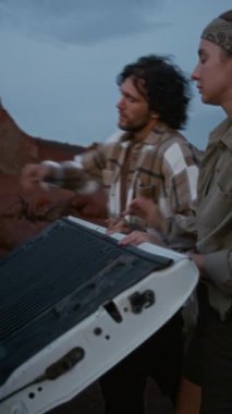 Beyaz bir kız ve adamın sırt çantalarını arabanın bagajından alıp yürüyüşe çıktıkları ya da yaz seyahatleri boyunca birlikte kamp yaptıkları orta boy dikey bir fotoğraf.