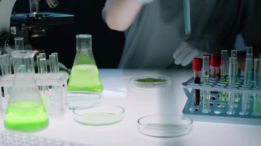 Tanımlanamayan laboratuar teknisyeninin ellerinin orta kesiminde mavi sıvı test tüpünü alıp, pipetini doldurup deney yapmak için petri kabında besleyici hücre kültürünün üzerine bırakması.