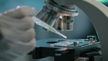 Tanımlanamayan bir bilim adamının elinde mikroskop altında pipetten numuneye bir damla sıvı eklendikten sonra laboratuvarda yapılan deney sırasında objektif bir göze dönüşüyor.