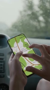 Genç bayan yolcuların dikey yakın çekimleri arabanın ön koltuğunda, yağmurda, akıllı telefondan haritayı gösteriyor, varış noktasına yaklaşıyor, ilerideki konumu gösteriyor.
