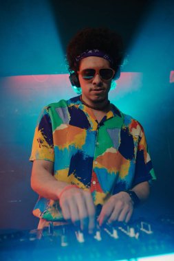 Hawaii tişörtü ve modaya uygun güneş gözlükleriyle genç ve şık erkek DJ 'ler gece kulübünde ses panosunun yanında durup sesleri karıştırıyor.