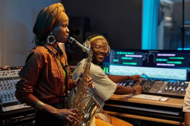 Musicians creating music in a recording studio with high-tech equipment. The saxophonist and producer concentrating on their work in a well-equipped, modern studio environment clipart