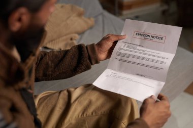 Elinde tahliye uyarısı tutan kişi, arka pencereden içeri giren ve loş bir odada doğal ışık olmadan kitap okurken...