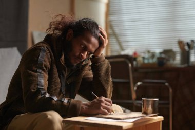 Düşünceli bir yüz ifadesi olan, başını kaldırıp elinde kalemle dizüstü bilgisayara bakan, konsantrasyonun derinlerine bakan bir adam.