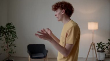 Z jenerasyonunun orta boy beyaz hardal tişörtlü adamı modern minimalist odada hızlı ve hareketli elleriyle konuşurken.