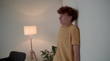 Hardal tişörtlü, duvarın karşısında duran ve yüzünü kapalı bir şekilde kapatan korkmuş beyaz bir adamın orta boy fotoğrafı.