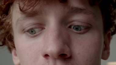 Gri gözlü, kızıl saçlı, gözleri için jimnastik yapan beyaz bir gencin aşırı yakın çekimi.