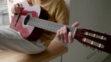 Yüzü olmayan bir adamın tahta pencere pervazında oturup kırmızı akustik gitarla şarkı çaldığı ve zamanını evde hobi yapmaya adadığı sahneler.