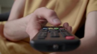 Televizyonun uzaktan kumandası çalışmadığı için düğmeye basan isimsiz kişinin eli kapalı, kapalı alanda kanal değiştirmeye çalışıyor.