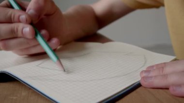 Kapalı bir masada oturan ve üniversite projesi için not defterine detay çizen isimsiz öğrencilerin el resimleri.