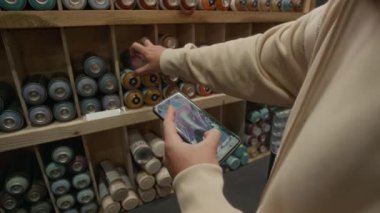 Bilinmeyen erkek graffiti sanatçılarının yeni sprey boyalar almak için alışverişe çıktıkları, akıllı telefon ekranında yeni proje tasarımına bakarken renkleri seçtikleri orta boy yakın plan çekimler.