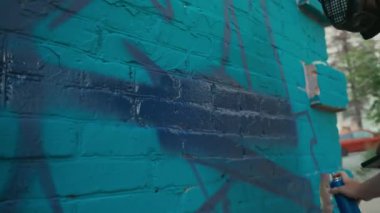 Genç erkek sokak ressamlarının ellerinde skeç ve boyama grafitileriyle duvara koyu mavi boyayla yazı yazarken, aynı zamanda kentsel alanda yeni bir duvar resmi üzerinde çalışırken