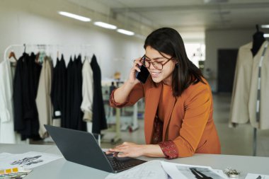 Modern atölyenin genç, gülümseyen bayan sahibi iş yerinde diz üstü bilgisayar ve danışmanlık müşterileri kullanırken