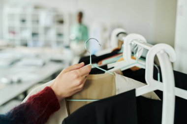 Genç erkek moda tasarımcısının eli ya da stilisti askıları askıdan yeni sezonluk kolleksiyondan, tamamlanmamış ceketle alıyor.