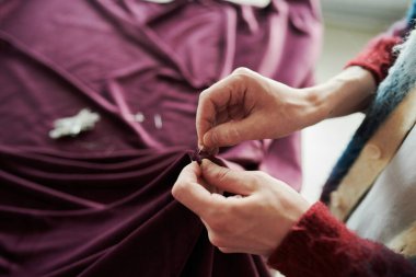 Genç, tanınmayan erkek terzinin yüksek açılı kolları, yeni kıyafetler yaratırken, pembeleşmemiş mor tekstilin kenarlarını iğnelemek.