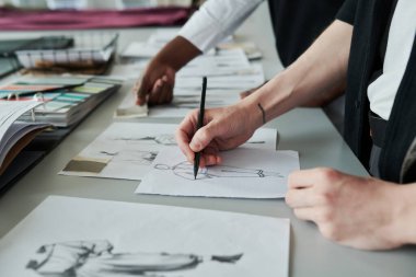 İş yerinin mevsimlik koleksiyonu için kalem çizimi yapan tanınmayan genç erkek moda tasarımcısının eli.