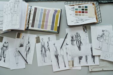 Yeni moda kıyafetlerin ve dikiş kalıplarının çizilmiş çizimlerinin üst görünümü, tekstil örnekleriyle dolu sepet ve kumaş örnekleri kataloğu