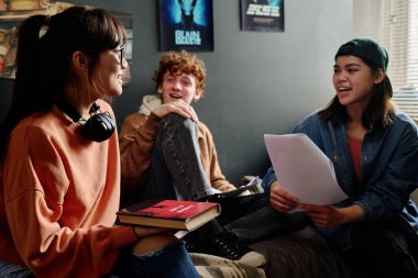 Proje üzerinde çalışan, günlük oda ortamında oturup tartışan, geniş gülümsemeli ve pozitif enerjili bir grup öğrenci.