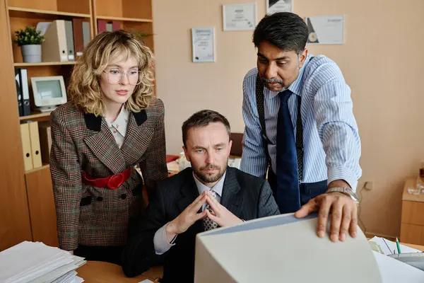 stock image Business professionals engaged in work discussion by computer in office. Individuals showing focused expression while analyzing and collaborating on project