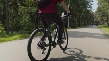 Güneşli yaz gününde, sırt çantalı ve orman yolunda gezen tanınmayan erkek bisikletçinin düşük açılı görüntüsü.