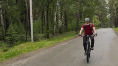 Orman yolunda bisiklet kaskı ve sırt çantası takan ve bisiklet süren son sınıf öğrencisi.