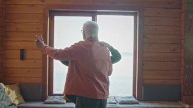 Aktif kıdemli beyaz çiftin gündüz vakti aydınlık pencerenin önünde dans ederken, hoş müziğin ritmine göre sallanırken, romantik bir anı paylaşırken.