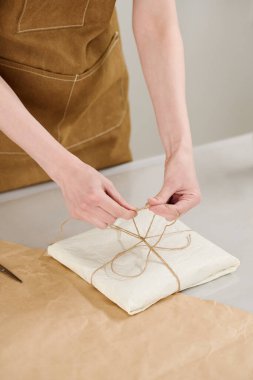 Kahverengi önlüklü, içinde yaratıcı sanat eserleri olan paketlenmiş ve paketlenmiş bir şekilde düğümlenmiş genç bir kadın.