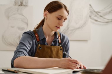 Yeni yaratıcı fikirleri düşünürken elinde kalemle defterin sayfasına bakan düşünceli genç bir kadın.