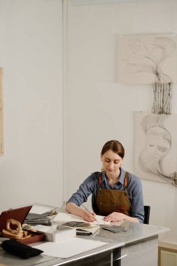 Genç, yaratıcı kadın iç mimar çizimlerini not defterine çizerken stüdyoda duvarlarda sanat eserleriyle otururken.