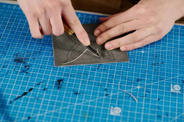 Tasarım stüdyosundaki iş yerlerinden kelebek desenlerini kesen el aletleriyle tanınmayan genç bir zanaatkarın yüksek açısı.