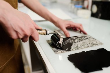 El yapımı sanat eserlerine siyah mürekkep uygulayan tanınmayan genç bir zanaatkarın elindeki küçük bir ressam.