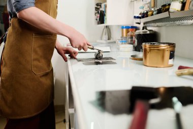 Önlüklü genç bayan tasarımcının tezgah başında durup küçük bir boyacıyla basılı sanat eserlerine mürekkep sürüşünün yan görüntüsü