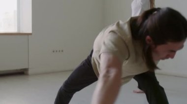 Profesyonel erkek dansçı, minimalist stüdyoda kadın partnerle prova yapmadan önce dinamik esneme egzersizi yapıyor.