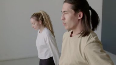 Genç, çok ırklı bir adam öne doğru eğiliyor, elleri arkada eğiliyor ve provadan önce kadın dans partneriyle ısınırken yavaşça yukarı doğru kıvrılıyor.