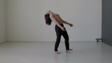 Uzun saçlı, kaslı, üstsüz bir adam stüdyoda prova yaparken ifade ile çağdaş bir şekilde dans ediyor.