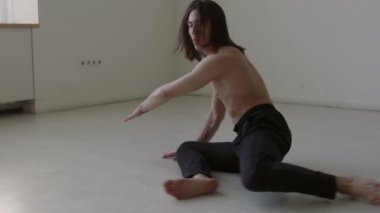 Gömleksiz vücutlu etkileyici erkek dansçı. Stüdyoda prova sırasında yer çalışması yapıyor.