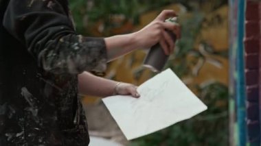 Gaz maskeli genç sokak sanatçısının yeşil sprey boyayla arka plandaki kırmızı-mor graffiti detaylarını çekerken yaz günü tuğla bina duvarını dekore ederken orta ölçekli bir fotoğrafı.